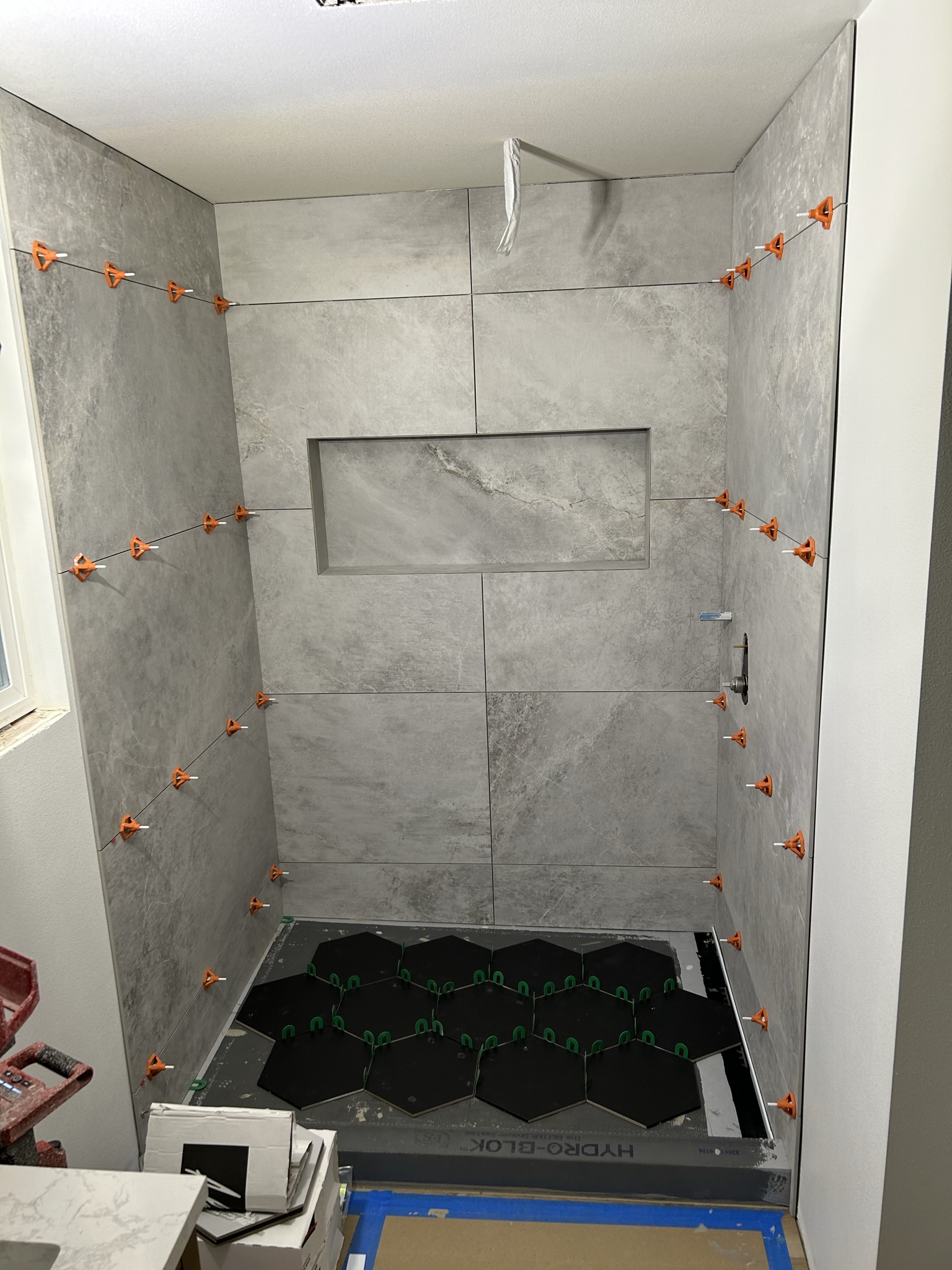 Gray shower wall tile installation nearing completion