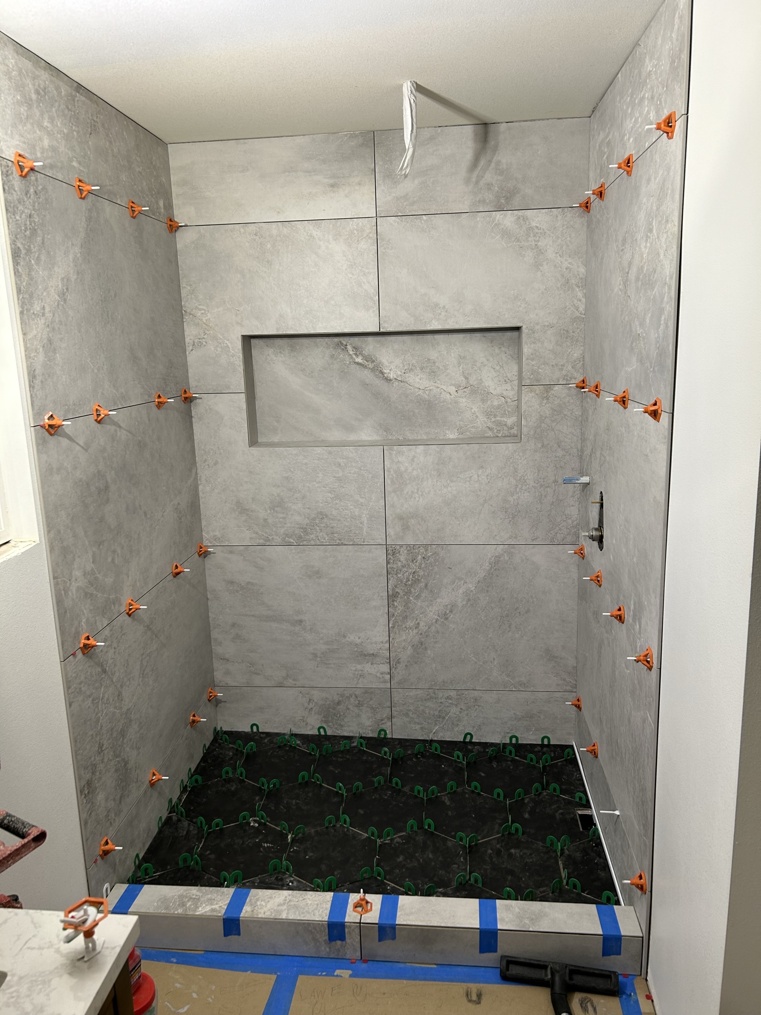 Shower wall tile and black hex floor tile installation in progress