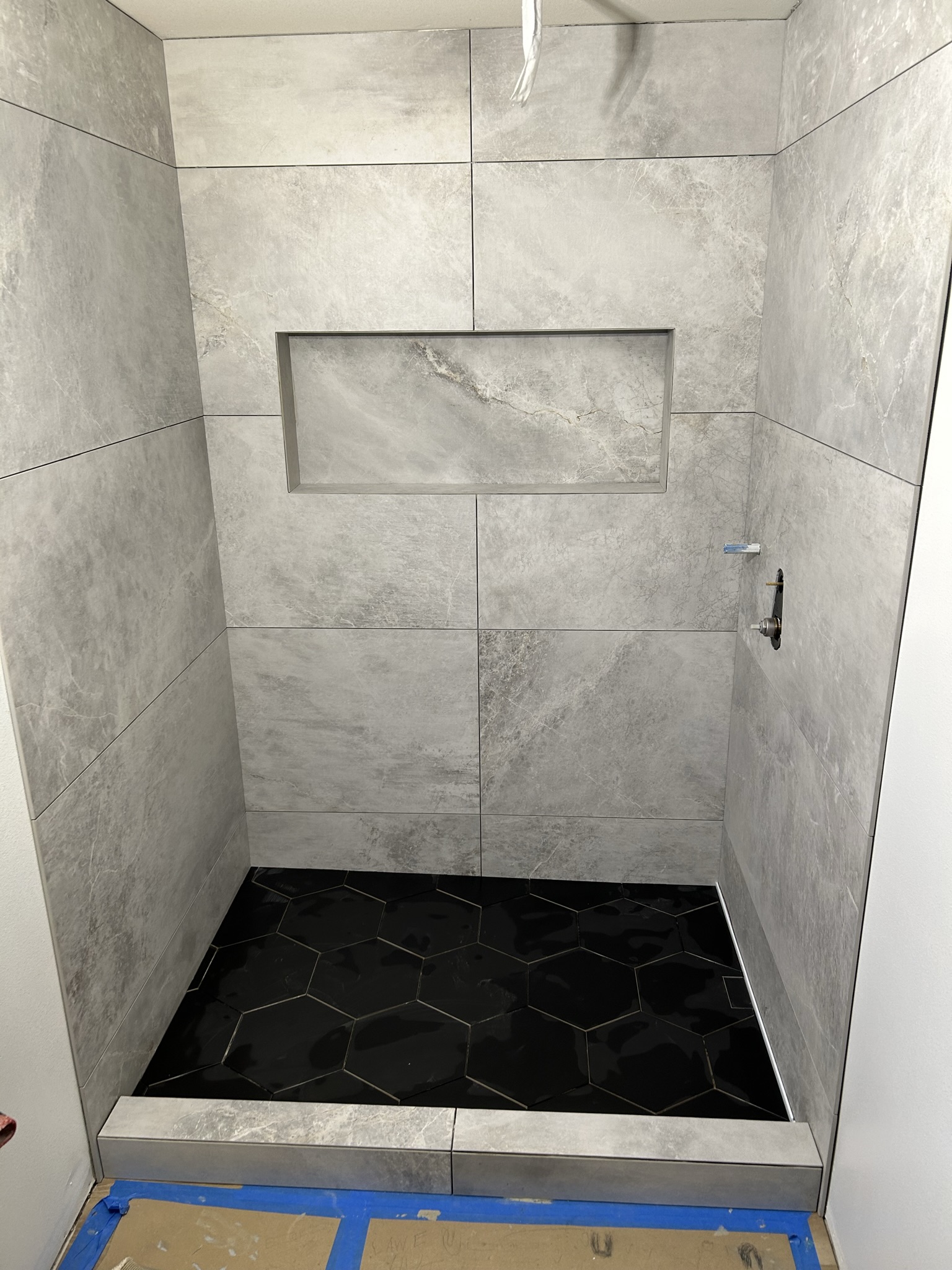 Completed tile walls, recessed niche, curb, and black hex shower floor