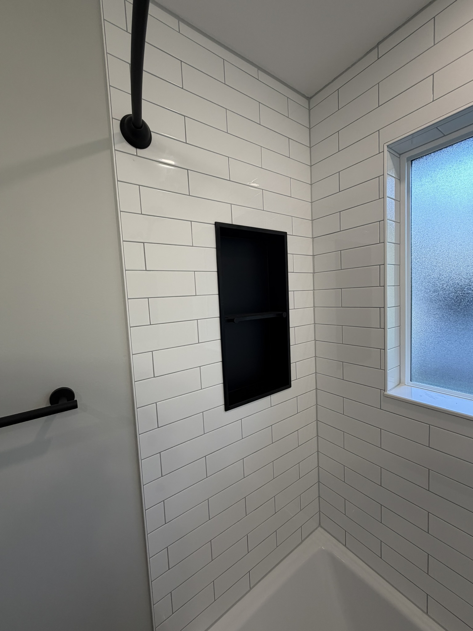 Recessed black shower niche set into the white tile surround