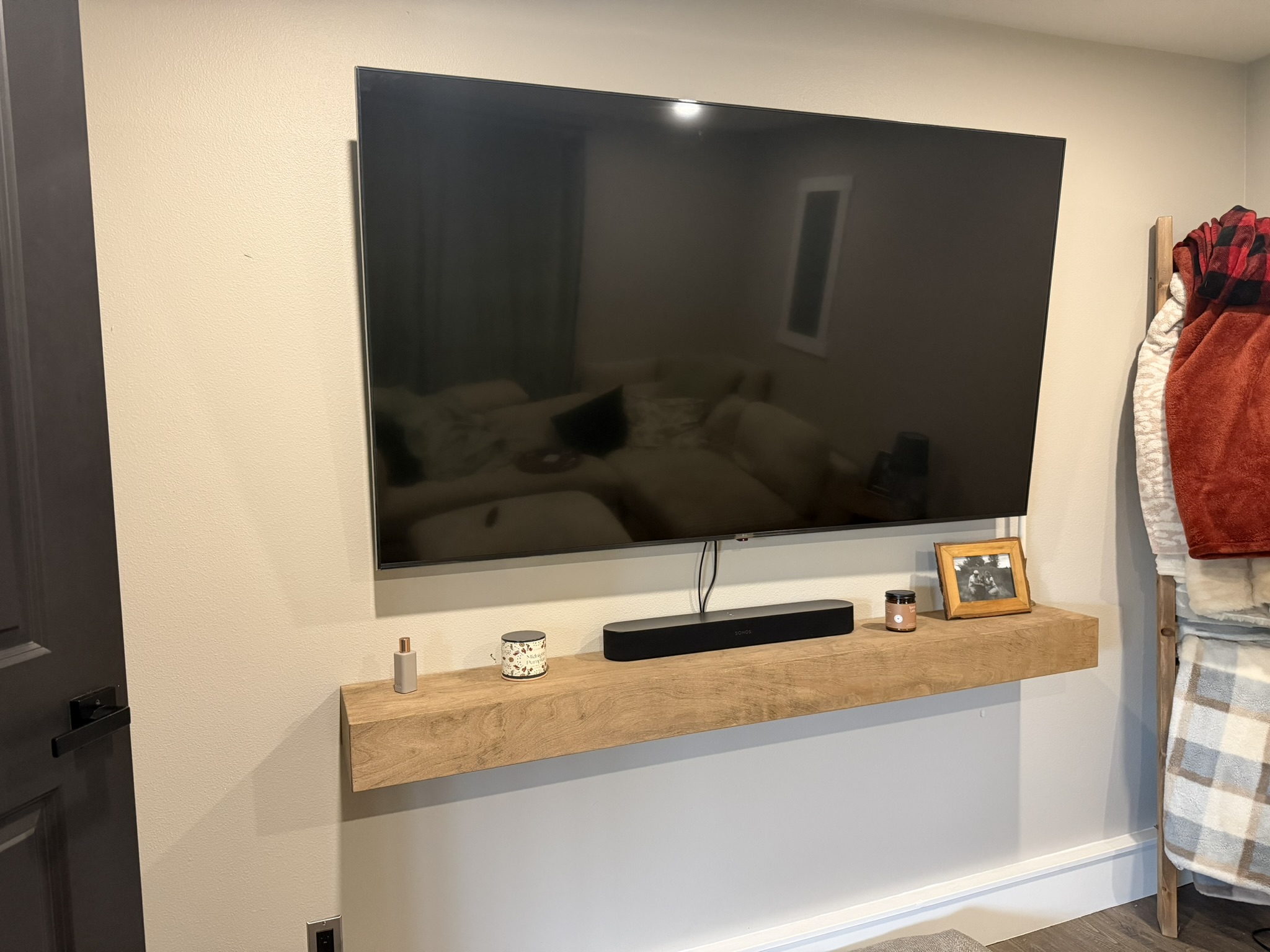 Finished custom wood floating media shelf installed below a wall-mounted television